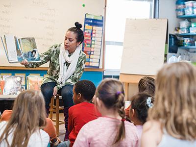一位实习教师坐在教室里给一群年轻的学生读一本绘本