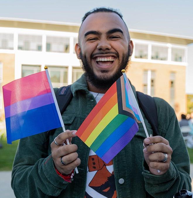 一名RWU学生拿着进步骄傲旗和双性恋骄傲旗对着镜头微笑