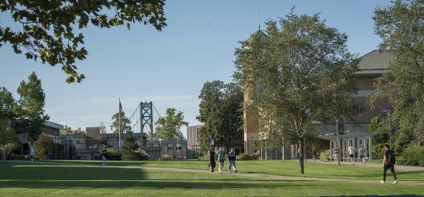 Students walk across RWU's Bristol Campus with Mount Hope Bridge and the American Flag in the background